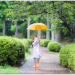 雨合羽を着て傘をさして歩く長くつの女の子